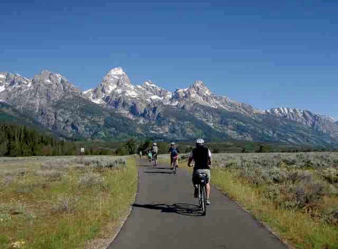 A paved path with cyclists, surrounded by mountains and greenery.