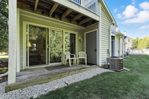 A covered porch with a wooden deck, two white chairs, and a trash can.