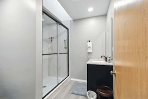 A modern bathroom with a glass shower enclosure, a dark vanity, and a wooden door.
