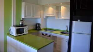 Een kleine keuken met witte kastjes, een groen aanrecht, een magnetron, een koffiezetapparaat en een koelkast.