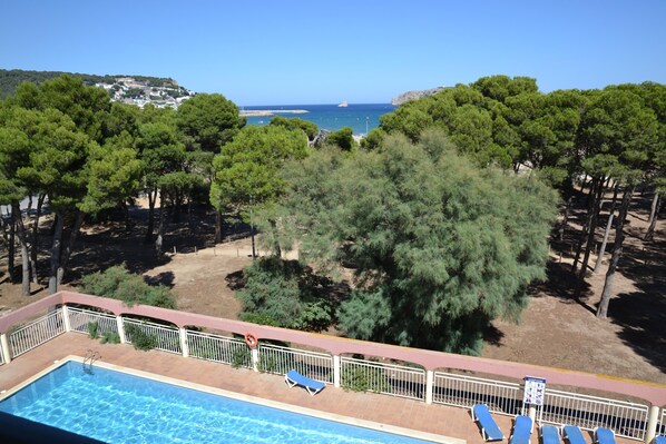 A swimming pool with lounge chairs, surrounded by trees and a view of the sea.