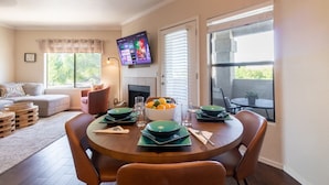 A dining area with a round table set for four, a television mounted on the wall, and a window with blinds. - Bright, Updated, Quiet N Scottsdale Escape (Scottsdale)