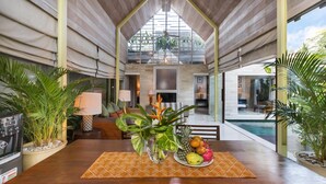Um quarto espaçoso com teto de madeira, área de jantar com mesa posta para dois e vista para uma piscina.
