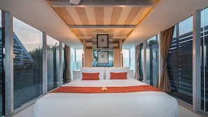 Quarto moderno com cama grande, vigas de madeira no teto e janelas amplas com vista para o exterior.