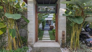 Um caminho leva a entrada de um edifício, cercado por plantas tropicais exuberantes.