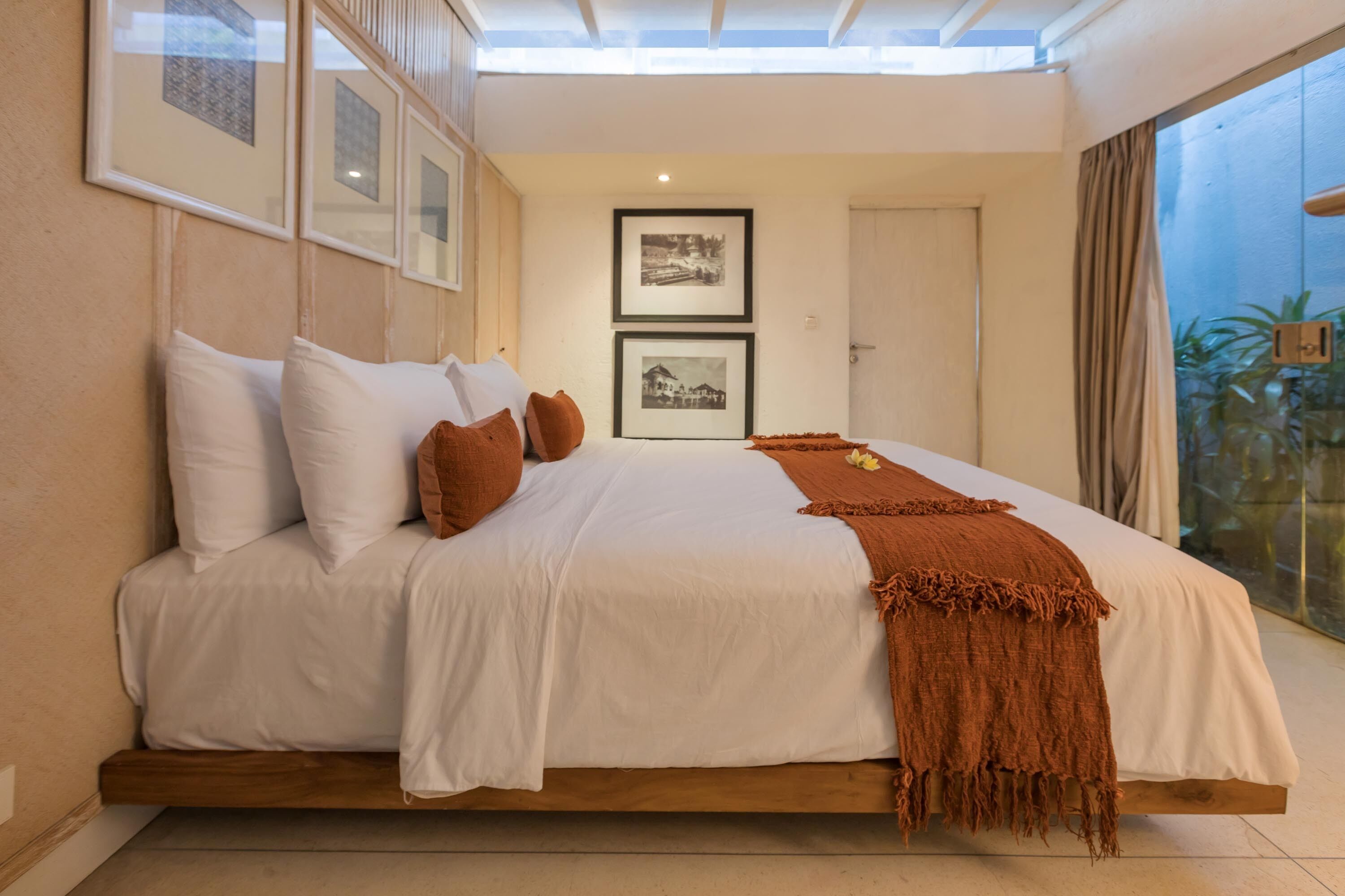 Una camera da letto con un letto grande, biancheria da letto bianca, una coperta marrone e quadri appesi al muro.