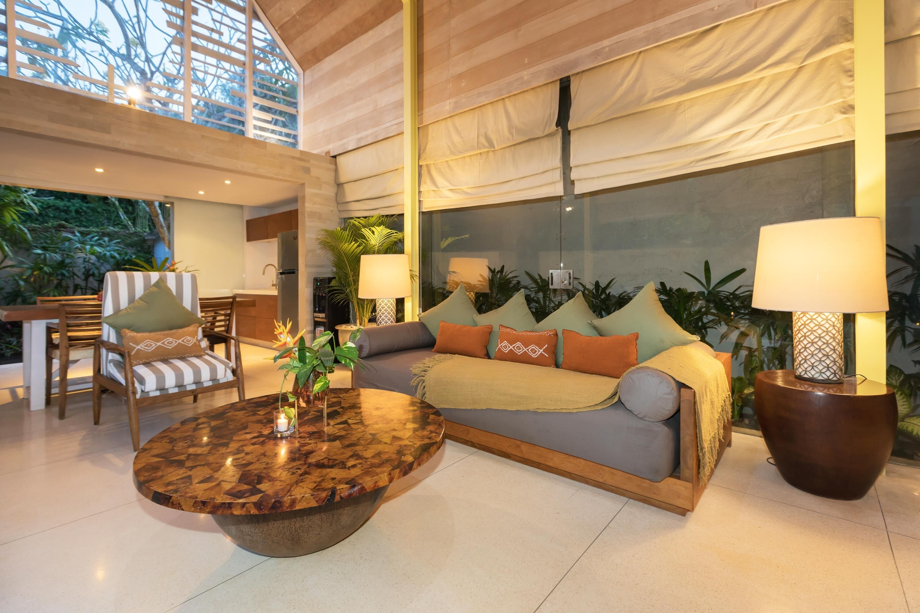 A spacious living area with a sofa, chairs, a coffee table, and a large window overlooking a garden.