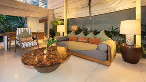 Ampla sala de estar com sofá, cadeiras, mesa de centro e uma grande janela com vista para um jardim.