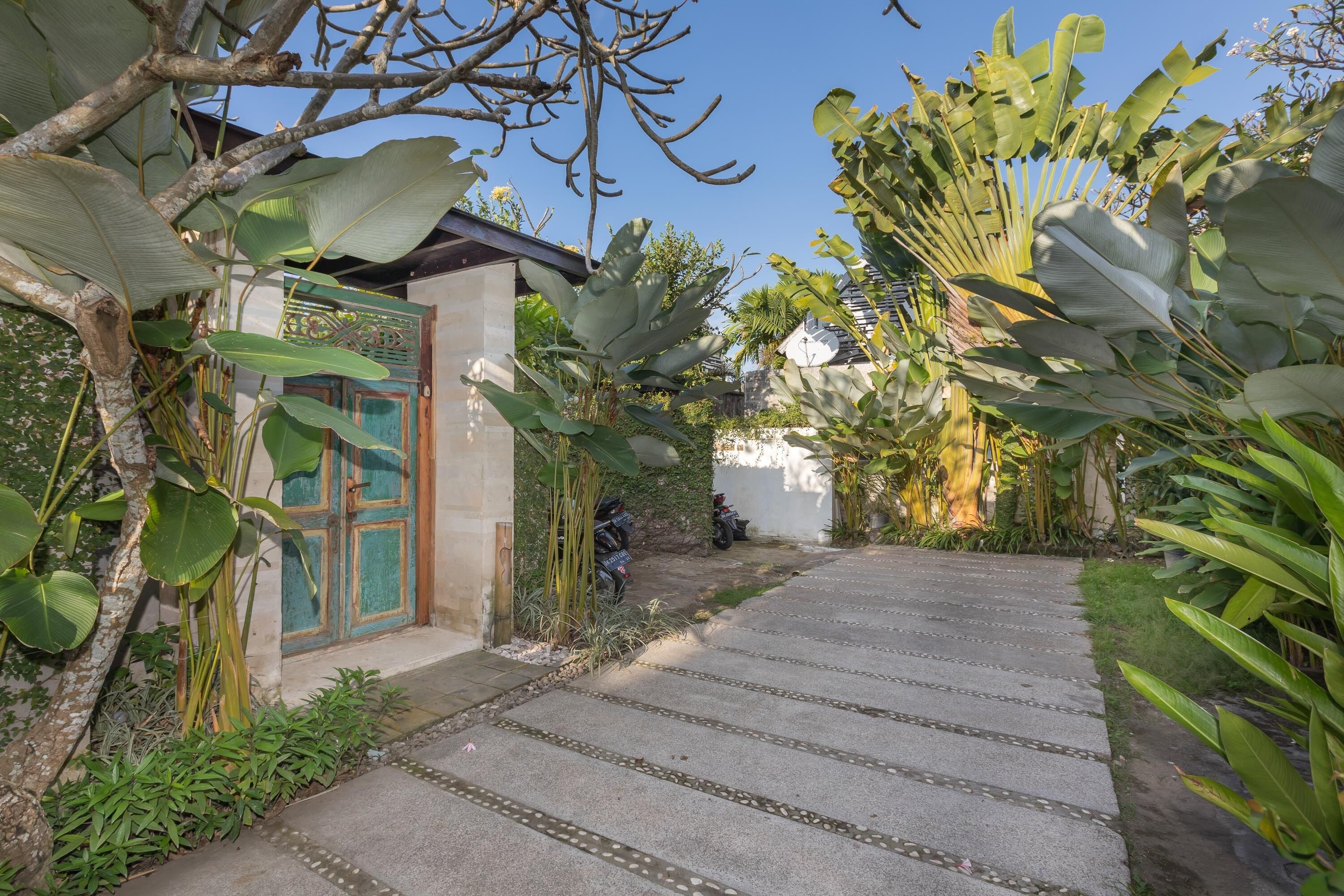 A pathway leading to a building with a decorative door, surrounded by lush tropical plants.