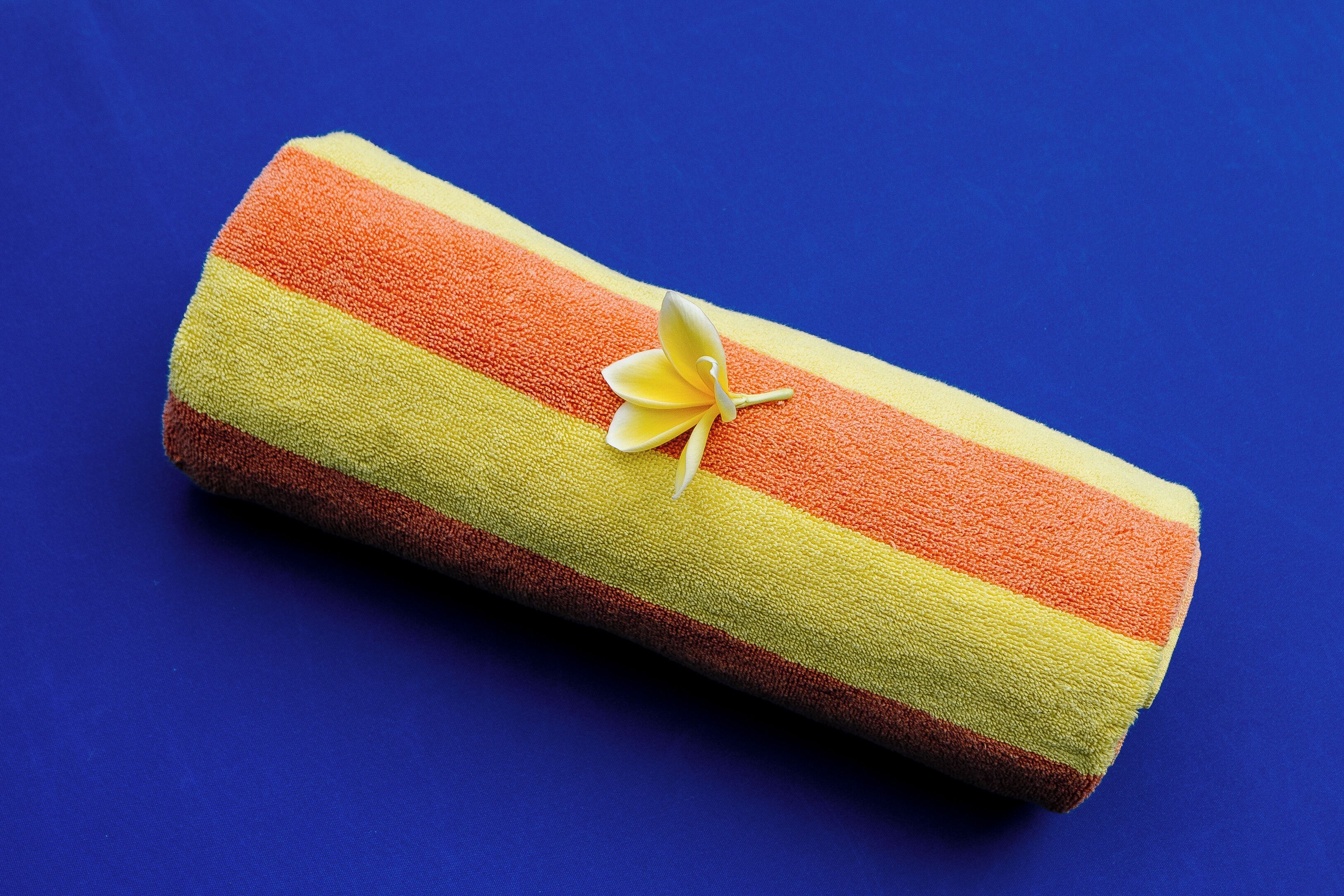 A rolled towel with a yellow flower decoration on a blue background.