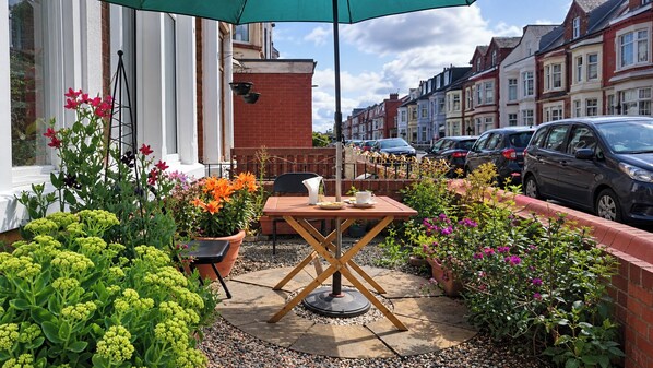 Un patio al aire libre con una mesa y sillas, rodeado de macetas con plantas y flores.