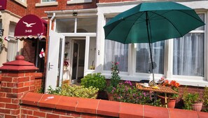 A residential property with a red brick facade, a white door, and a green umbrella providing shade. - Central 4-Bed Home, Sleeps 9 with Parking & Spa (Blackpool)