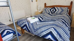 A bedroom with a bunk bed, a bedside table with a lamp, and a patterned bedspread.