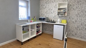 A compact kitchen with a microwave, a small refrigerator, and a shelf unit with kitchenware. - Central 4-Bed Home, Sleeps 9 with Parking & Spa (Blackpool)