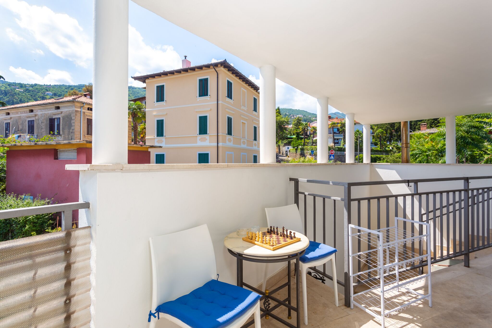 A balcony with a chessboard, white chairs, and a metal rack.