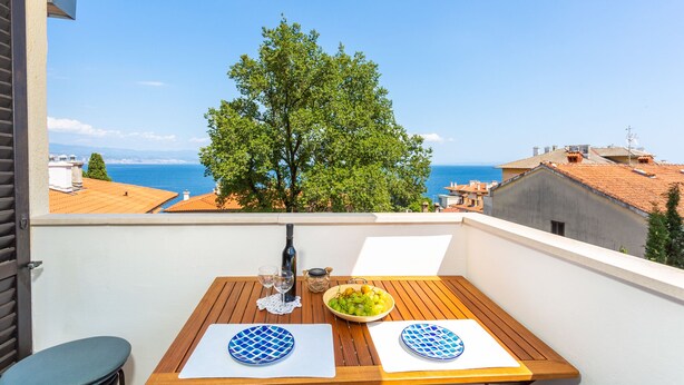 Ein Balkon mit einem Tisch für zwei Personen, einer Flasche und einer Schüssel mit Obst.