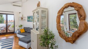Ein modernes Wohnzimmer mit Ecksofa, einer Glastruhe, einem Holzsessel und Blick auf den Balkon.