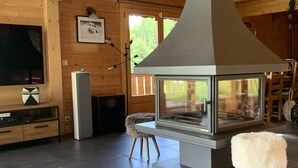A modern living room with a large fireplace, wooden walls, a television, and a cozy rug. - Beautiful 5-bed chalet in Les Carroz d'Araches (Les Carroz d'Araches)