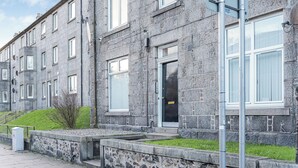 A stone building with multiple windows and a door, a small grassy area, and a metal pole with a sign. - Cosy Central Aberdeen 1 Bed Flat by Retail Park (Aberdeen)