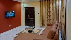 A living room with a sofa, a television mounted on the wall, a ceiling fan, and a patterned rug.