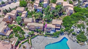 Eine Vogelperspektive eines Wohngebiets mit mehreren zweistöckigen Gebäuden, einem Swimmingpool und umgebender Bepflanzung.