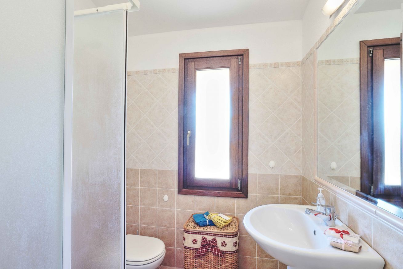 A bathroom with a toilet, a sink, and a shower. There is a window above the toilet and a mirror above the sink.