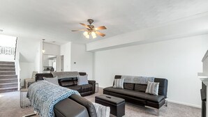 A spacious living room with a large brown leather sofa, a smaller sofa, and a coffee table. There is a ceiling fan and a staircase leading to another level. - Comfortable 3 - Bedroom Norfolk Stay  – Minutes from Bases and ODU (Norfolk)