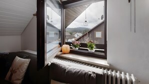 Una habitación con vista a una casa, una ventana con vista a una montaña, un radiador y un cojín con diseño de ciervo.