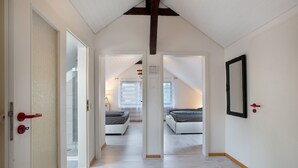 Un pasillo que conduce a dos dormitorios con paredes blancas y techo de madera, y una puerta con pomo rojo.