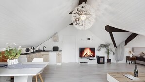 Un espacio habitable moderno con cocina, comedor y zona de estar, que cuenta con una chimenea, paredes blancas y una lámpara de techo única.