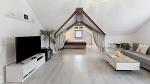 Une chambre de style loft moderne avec un plafond en pente, une télévision, un canapé, une table basse et une bibliothèque.