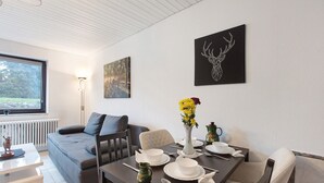 A modern dining area with a table set for four, a sofa, and a window with a view of trees.