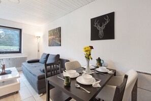Un espace de repas moderne avec une table dressée pour quatre personnes, un canapé et une fenêtre donnant sur un paysage arboré.