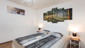 A bedroom with a bed, a nightstand, a wall-mounted light, and a painting.