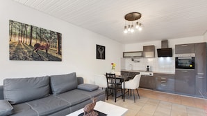 A modern kitchen with a dining area, a gray sofa, and a painting of a deer.