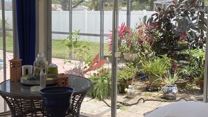 Ein Wintergarten mit einem Glastisch und Stühlen, umgeben von Topfpflanzen und Blick auf eine Wohngegend.