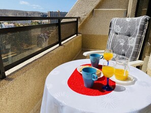 Un balcon avec une table préparée pour le petit-déjeuner, comprenant des croissants, une tasse bleue, un verre de jus d’orange et un verre d’eau.