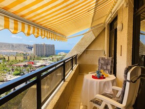 Un balcon avec un auvent rayé, une table avec des aliments pour le petit-déjeuner et une chaise.