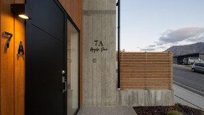 A modern building entrance with a concrete facade, a wooden slatted fence, and a clear view of a mountain range in the background.