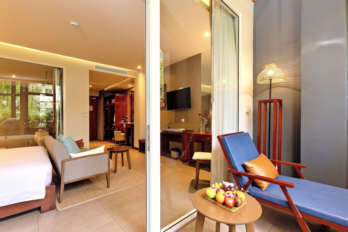 A hotel room with a bed, a seating area with a chair and a table, and a TV mounted on the wall.