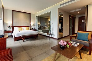 Une chambre d’hôtel moderne avec un grand lit, un canapé, une table basse agrémentée de fleurs et de livres, et un miroir qui reflète la pièce.