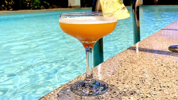 Een cocktail met ananasdecoratie bij een zwembad.