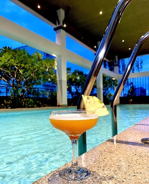 A cocktail with a pineapple garnish by a poolside.