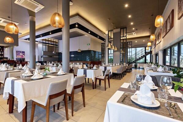 A spacious dining area with multiple tables set for dining, large windows offering views, and a modern interior design.