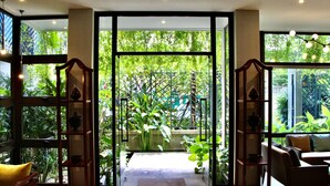 Een kamer met een grote glazen deur die uitkomt op een tuin, houten meubels en uitzicht op groen.