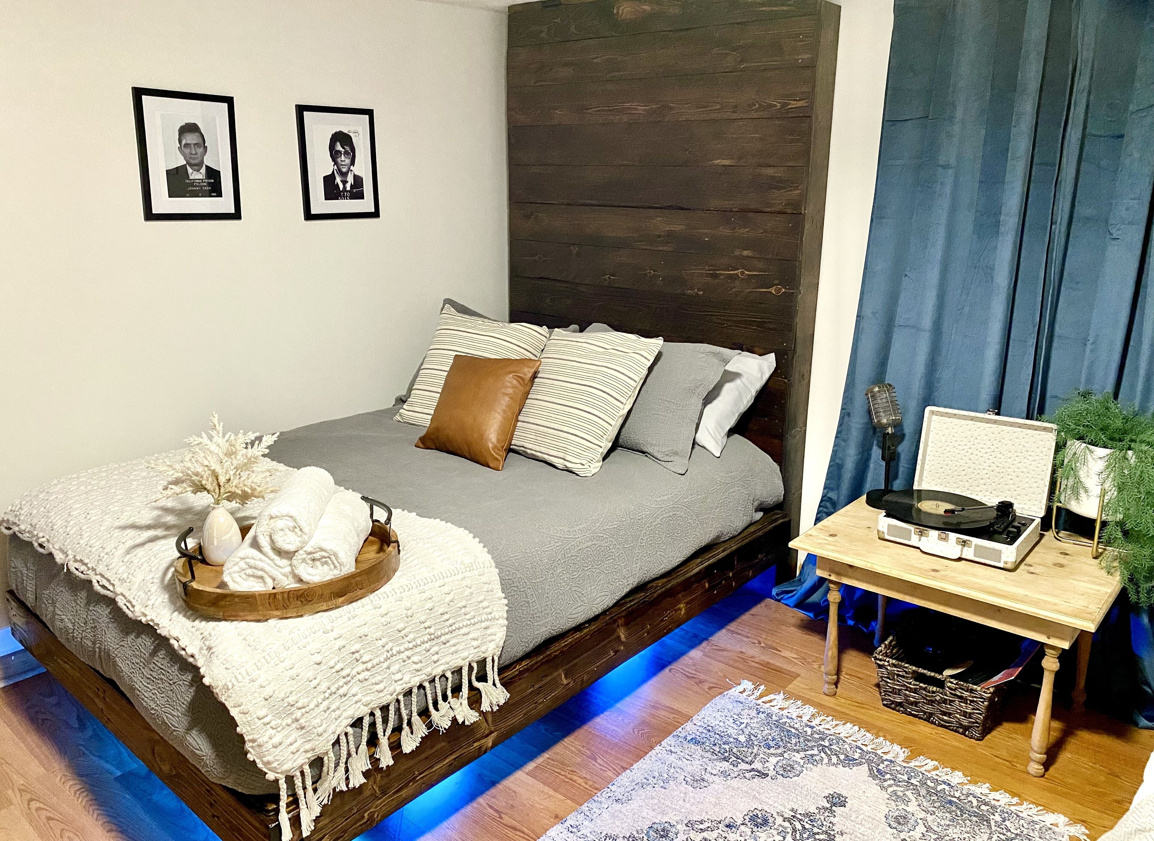 A modern bedroom with a bed, pillows, a bedside table with a record player, and a small plant.