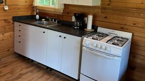 A compact kitchen with wooden walls, a gas stove, white cabinets, and a window with curtains.