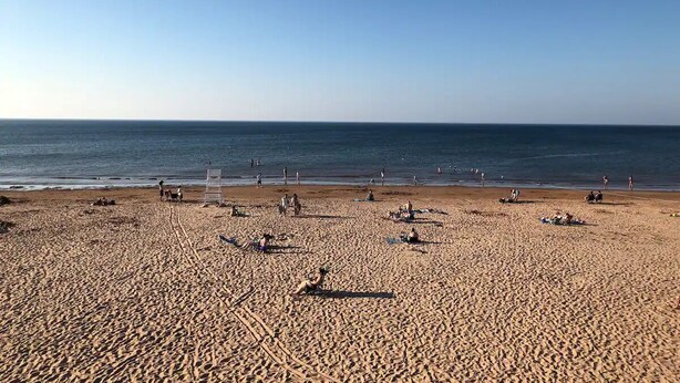 A wide sandy beach with a clear sky, several lifeguard stands, and people scattered across the sand.