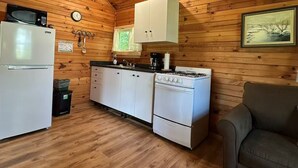 A compact kitchen with wooden walls, a white stove, a microwave, and a refrigerator.