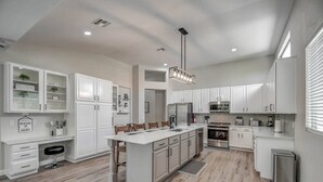 A spacious kitchen with white cabinetry, a central island, and a stainless steel refrigerator.